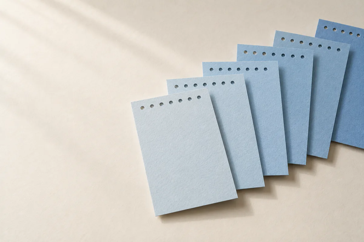Seis tarjetas azul claro se despliegan en abanico, de tonos claros a oscuros, con los agujeros superiores alineados.