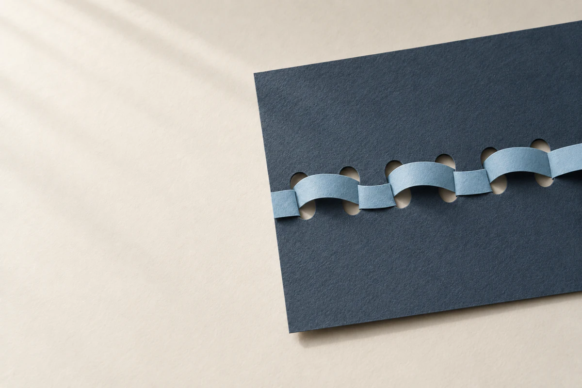 Durch eine Reihe runder Löcher in dunkelblaugrauem Papier läuft ein hellblauer Streifen abwechselnd hindurch.